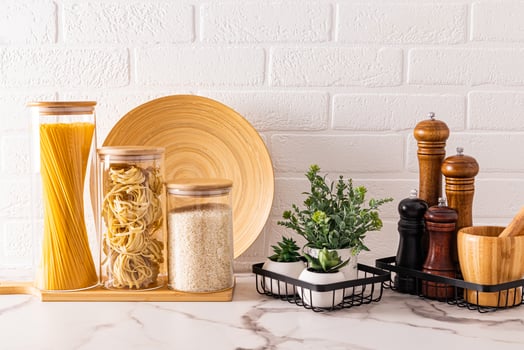 A set of jars for bulk products and various spice grinders on a marble countertop with beautiful plants in pots. Space-saving storage. Front view photo