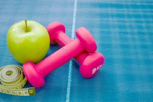 Two red dumbbells, an apple and a centimeter ribbon on a yoga mat. Concepts about fitness, sport and health. photo