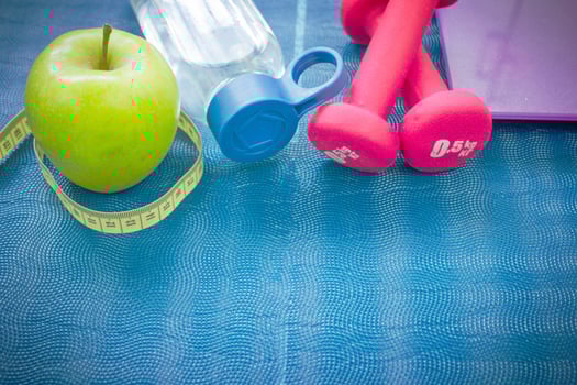 Two red dumbbells, an apple, a tape measure, a bottle of water and weight scales on a yoga mat. Concepts about fitness, sport and health photo