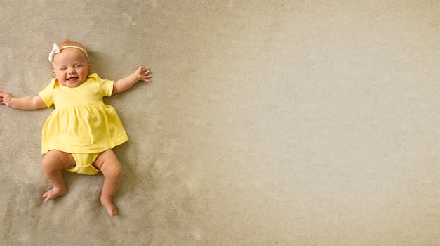 Cute, sweet and charming little girl in a yellow bodysuit lying on the bed and smiling. photo