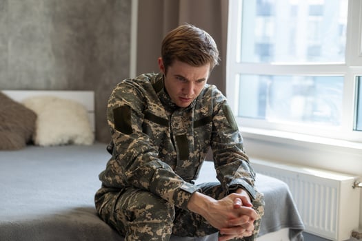 Stressed veteran soldier engrossed in depressive thoughts and memories. Sad depressed young military man in camouflage uniform sitting on couch and thinking about war. PTSD and therapy concept. photo