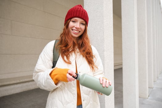 Beautiful redhead woman drinking hot tea or coffee from thermos, female tourist enjoys warm drink, rests during her journey around town photo