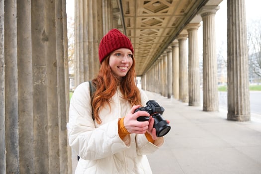 Smiling tourist photographer, takes picture during her trip, holds professional camera and makes photos