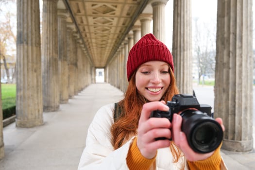 Smiling tourist photographer, takes picture during her trip, holds professional camera and makes photos