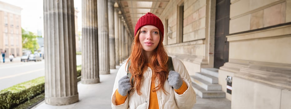 Smiling redhead girl with backpack, walks in city and does sightseeing, explore popular landmarks on her tourist journey around Europe photo