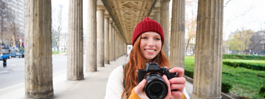 Smiling tourist photographer, takes picture during her trip, holds professional camera and makes photos