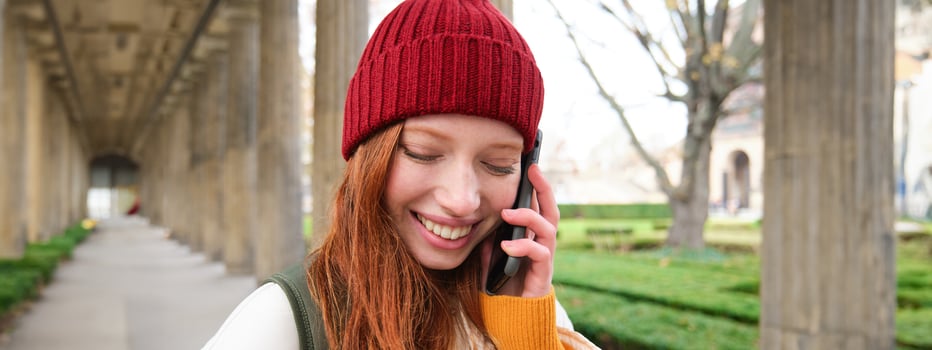 Portrait of redhead european girl in red hat, makes a phone call, walks in city and talks to friend on smartphone photo