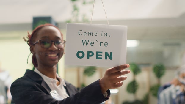 African american employee opening clothing store in the morning, waiting for customers. BIPOC retail worker turning closed message sign on fashion boutique door in shopping center photo