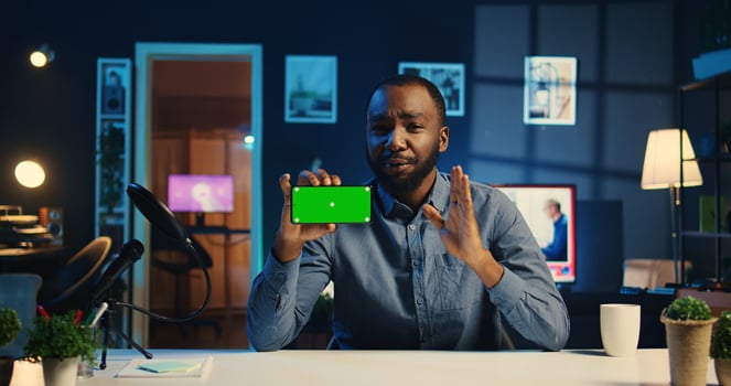 Happy content creator holding chroma key product, being sponsored by tech company to film unboxing review. African american influencer showing mockup screen phone recommendation to viewers photo