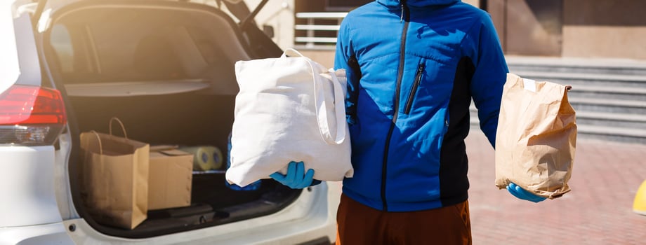 Delivery man holding paper bag with food near the car, food delivery man in protective mask photo