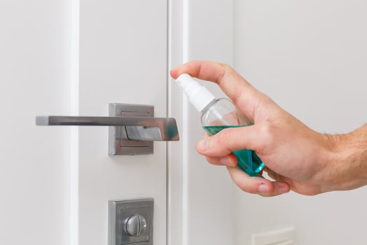 Hands hold the sprayer with an antiseptic, the other - wipes the door handle with a cloth moistened with a disinfectant solution photo