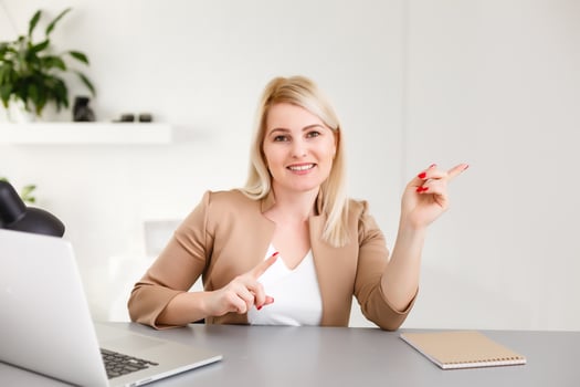 beautiful business woman smile sitting at the desk looking at camera, point finger at isolated white laptop screen over white background photo