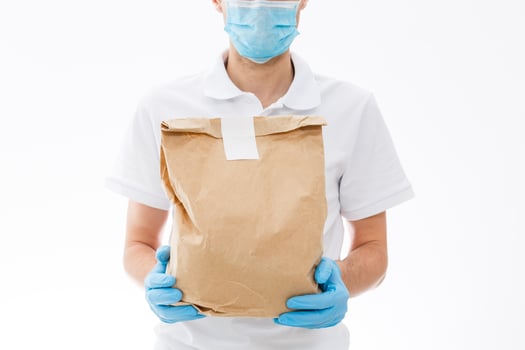 Courier in protective mask and medical gloves delivers takeaway food. Delivery service under quarantine, disease outbreak, coronavirus covid-19 pandemic conditions. photo