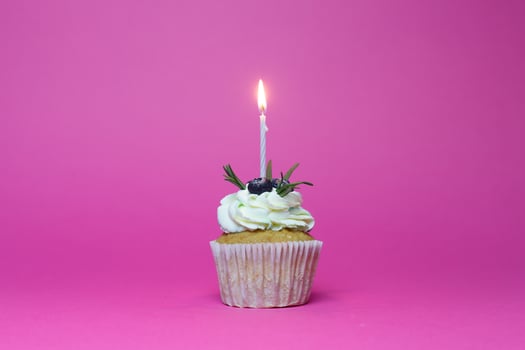 birthday cupcake with one burning candles over pink background photo