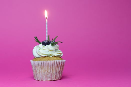 birthday cupcake with one burning candles over pink background photo