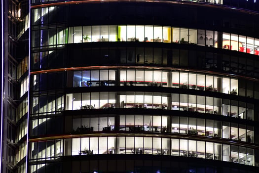 Fragment of the glass facade of a modern corporate building at night. Modern glass office  in city. Big glowing windows in modern office buildings at night, in rows of windows light shines. photo