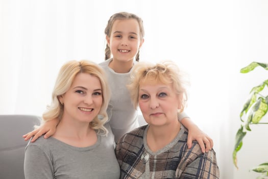 Three generations of women. Beautiful woman and teenage girl are kissing their granny while sitting on couch at home photo
