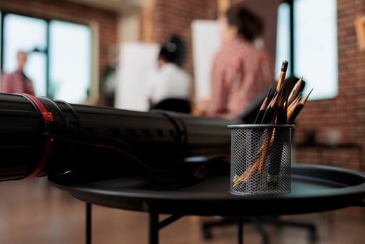 Pencils in metal holder and canvas tube on table in modern art studio, drawing tools and supplies in classroom. People learning to draw and sketch in group, fine arts education photo
