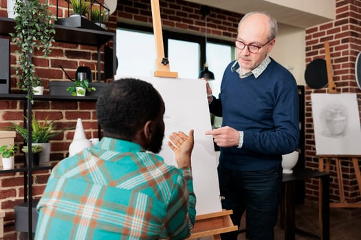 People connecting while learning new skills, two diverse men looking at easel with canvas discussing artwork while studying pencil drawing together at group art class. Sketching lesson photo