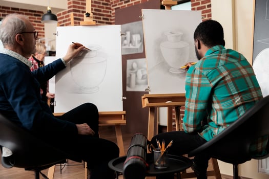 Rear view of two diverse men students sitting at easels practicing still life drawing in art studio. Friends learning new things together, people learn how to draw with pencil during creative workshop photo