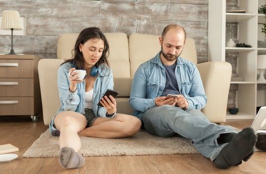 Couple using smartphone while sitting on living room rug. photo