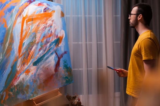 Artist holding paint brush looking at colorful painting in art studio. Modern artwork paint on canvas, creative, contemporary and successful fine art artist drawing masterpiece photo