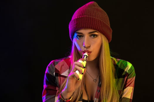 Vaping girl. Young hipster woman vape e-cig on studio on black background. Hip-hop style. Close up. photo