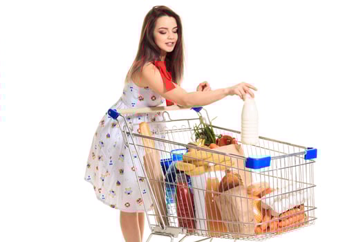 Smiling young woman doing grocery shopping at the supermarket, she is putting a milk bottle in the cart photo