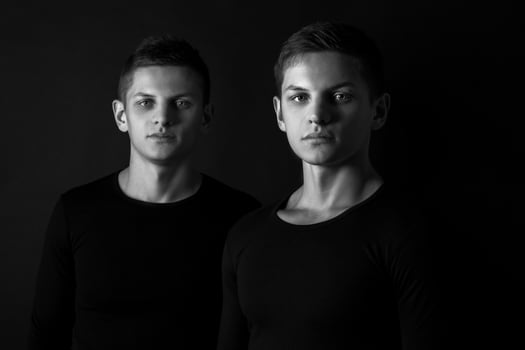Two attractive positive young twin brothers standing dressed in photo