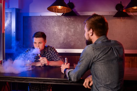 Vaping man holding a mod. A cloud of vapor at the vapebar. photo