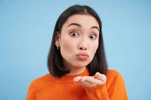 Close up of beautiful asian woman sends air kiss at camera, stands over blue background photo