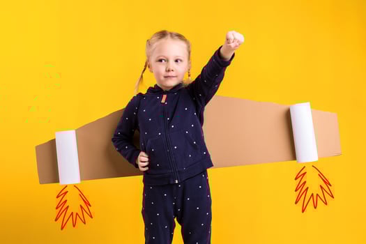 A little child girl is wearing homemade cardboard flying wings, pretending to be a pilot for a craft, imagination or exploration concept. photo