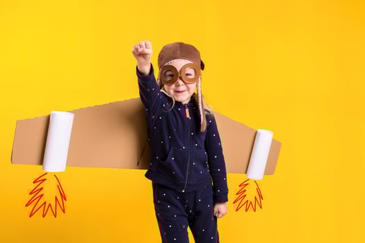 Freedom, girl playing to be airplane pilot, funny little girl with aviator cap and glasses, carries wings made of brown cardboard as an airplane photo