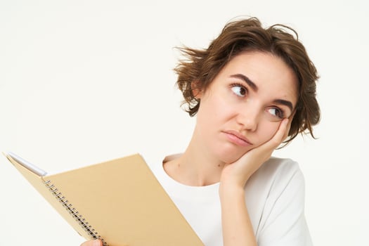 Portrait of tired and bored student, woman reading her notes, doing homework, holding notebook planner and grimacing, standing sad against white background photo