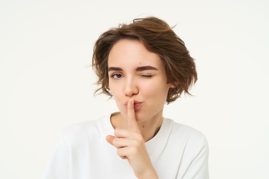 Close up shot of cute girl, press finger to lips, makes shhh shush noise, keeps secret, stands over white background photo