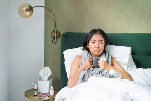 Sick sad asian girl lying in her bed with flu, catch a cold, taking pills and drinking hot tea, feeling upset photo