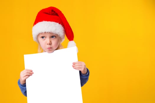 Cute little girl in Santa Claus hat with a white blank paper sheet. Christmas, x-mas, New Year, Winter, people, advertisement, sale concept. photo