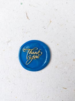 Blue button wax coin with the gold word thank you on it on a white background photo