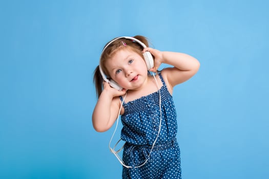Cute little girl in headphones listening to music using a tablet and smiling on blue background photo