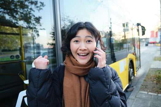 Happy asian girl talks on mobile phone and looks surprised, amazed by great news, achieve goal, hear something exciting photo