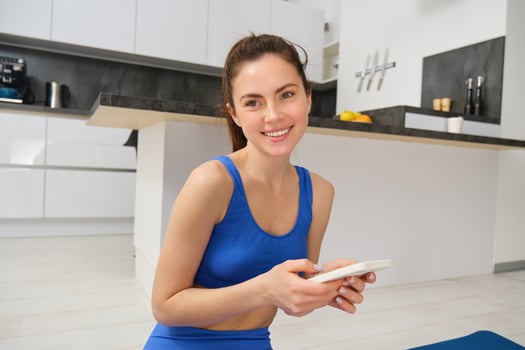 Close up portrait of sporty girl in sportsbra, holds smartphone, workout from home, looking at exercises on mobile phone photo