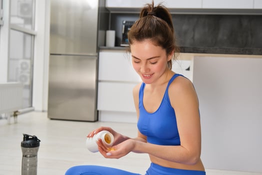 Image of young woman, sporty fitness girl taking vitamins, dietary supplements for muscles strength, sitting on yoga mat and workout photo