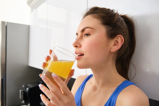 Beautiful woman drinking an organic orange juice. Fit young woman drinking from glass. Healthy girl enjoy detox drink and looking away photo