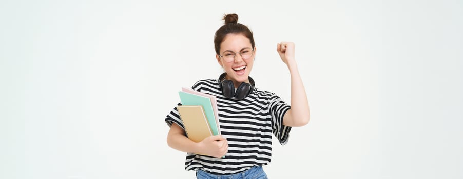 Enthusiastic young woman in glasses, teacher celebrating, raising hand up and cheering, tirumphing with joyful smile, white background photo