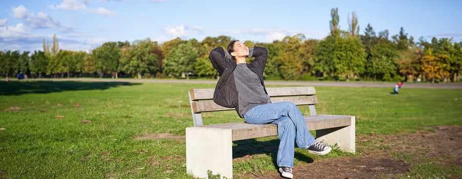 Portrait of happy asian girl feeling freedom and excitement, stretching hands while sitting on bench and smiling photo