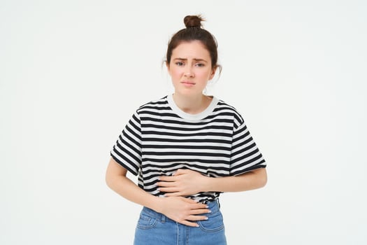 Woman feeling hungry, touching her belly. Girl with period cramps, menstrial pain, holds hands on stomach that aches, isolated over white background photo