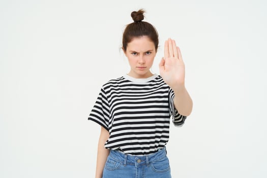 Image of serious and confident young woman, shows stop sign, taboo gesture, prohibit something bad, standing over white background photo