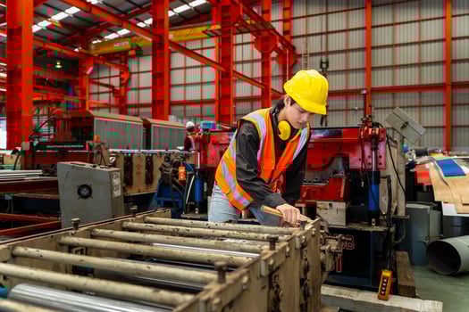 Asian industrial worker is checking the setup value of metal sheet roll forming machine inside roof factory for safety industry construction concept photo