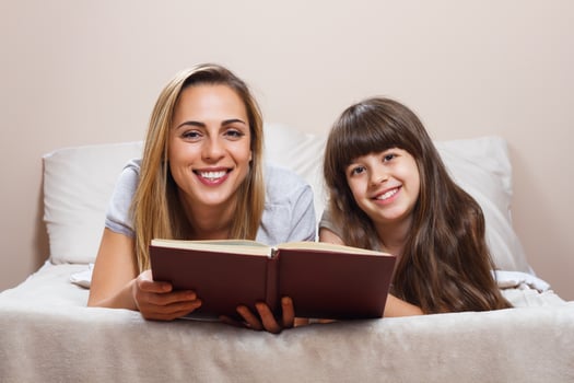 Mother and daughter reading together book in bed photo