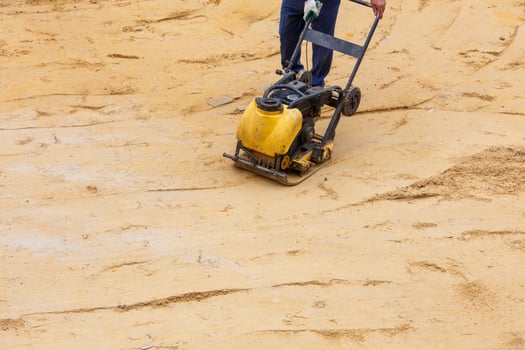 Worker using vibratory plate compactor for compaction sand during path construction. photo